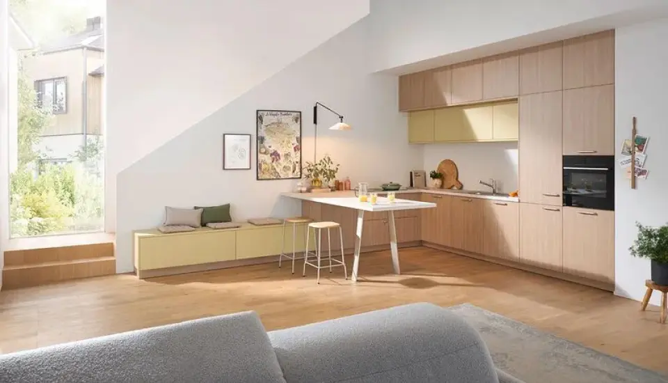 Offene Wohnküche im Dachgeschoss mit hellen Holzfronten, integrierter Zeile und kleinem Esstisch; große Fensterfront, Sitzbank mit Stauraum, warme Farbakzente und viel Tageslicht in modernem, gemütlichem Ambiente.